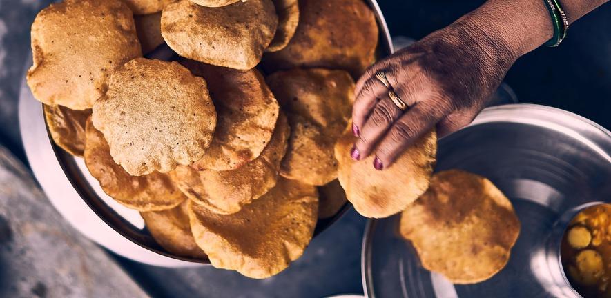 Someone reaching for a puri from a bowl full of this delicious Indian food.